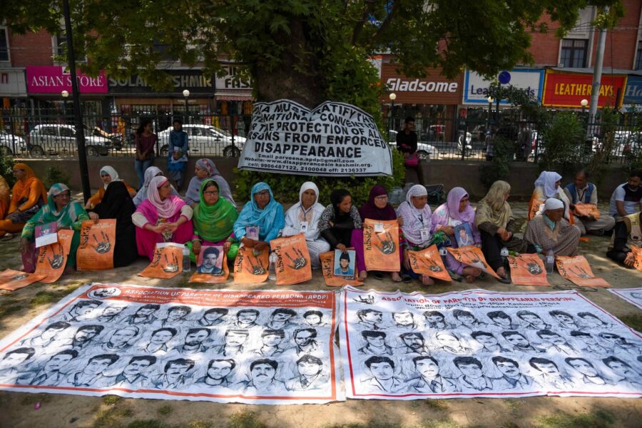 Kvinder i Kashmir sidder foran plakater af forsvundne mænd.