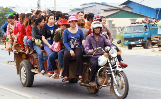 Plaggfabrikkarbeidere fra Kandal-provinsen i Kambodsja kjører hjem i en «romork» – et kjøretøy laget av motorsykkel og små lastebildeler – for å komme hjem.