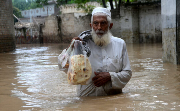 En mann bærer brød gjennom en flommet gate i Peshwar.
